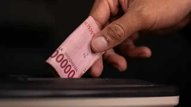 Tangan menyelipkan lembaran rupiah ke celah kotak