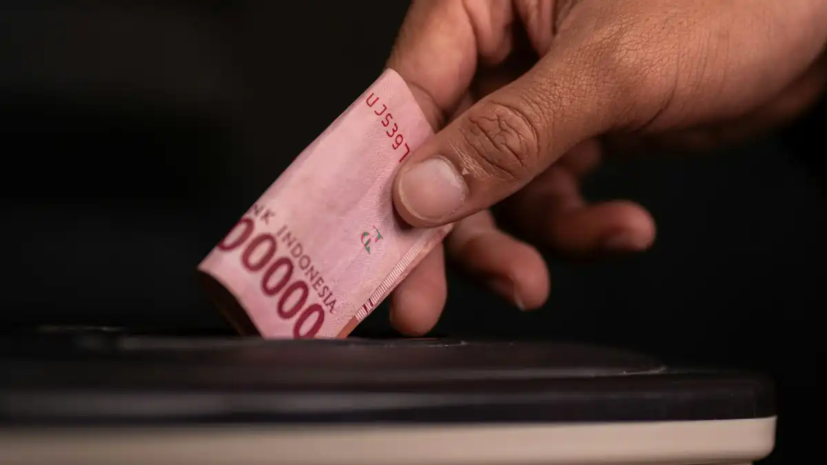 Tangan menyelipkan lembaran rupiah ke celah kotak
