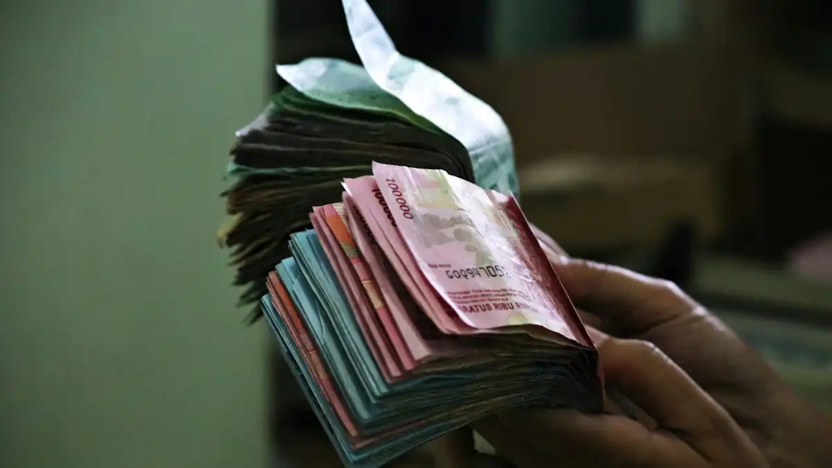 Tangan memegang uang rupiah dalam jumlah besar