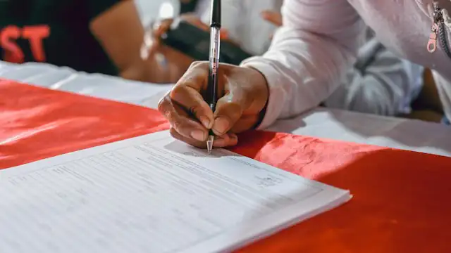 Tangan menulis di atas kertas di meja bertaplak merah