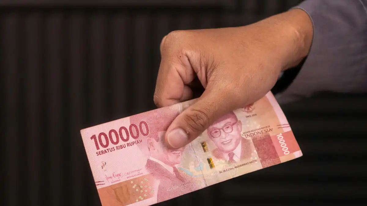 Tangan menyerahkan uang rupiah pecahan seratus ribu