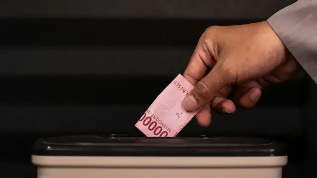 Tangan memasukkan uang rupiah ke celah kotak